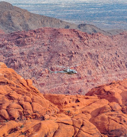 Helicopter over glowing red rock formations with the Las Vegas valley in the background